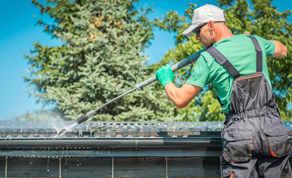 Roofing professional cleans a house's gutters from a ladder