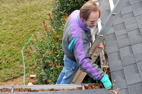 Man on a ladder cleaning gutters at a corner of the roof