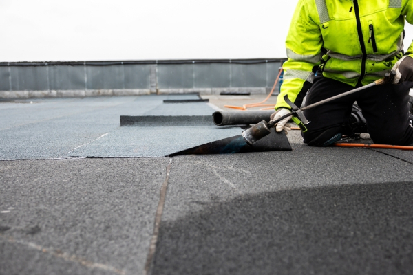A contractor lays down a bitumen membrane on a commercial roof.