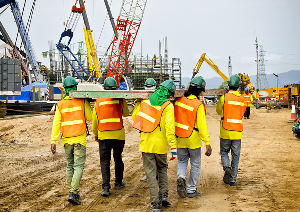 A construction crew walks across a jobsite with cranes in the background
