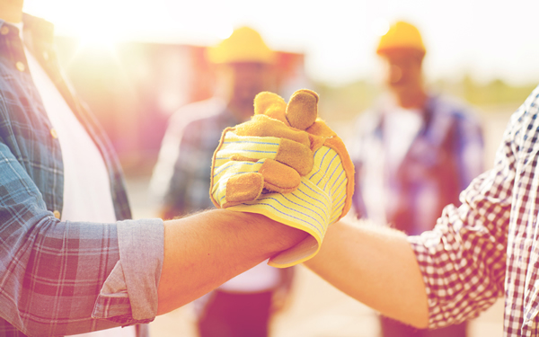 Two construction workers leaning in for a handshake