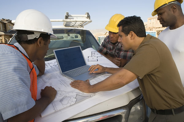 Contractors crowding around a laptop propped on a truck hood