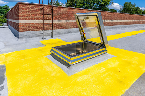 An open roof hatch surrounded by yellow warning paint without guardrails.