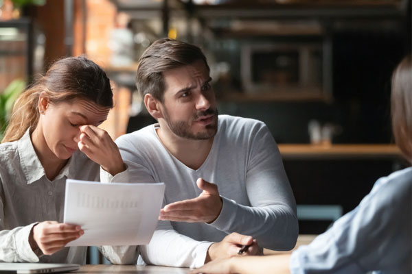 Two frustrated clients complaining to a contractor at a desk.