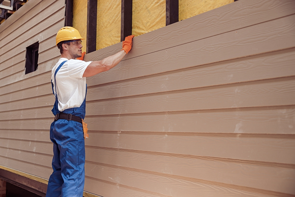 A construction worker installs siding on a house.