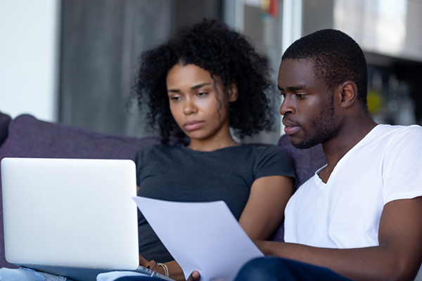A young couple (man and woman) reviews information on a laptop and looks at documents.