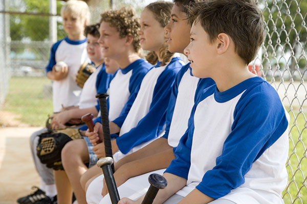 a group of five youths sitting on a bench in the dugout wearing blue and white baseball uniforms