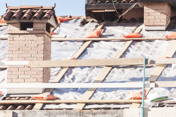Emergency repair in progress of a tile roof with plastic sheeting.
