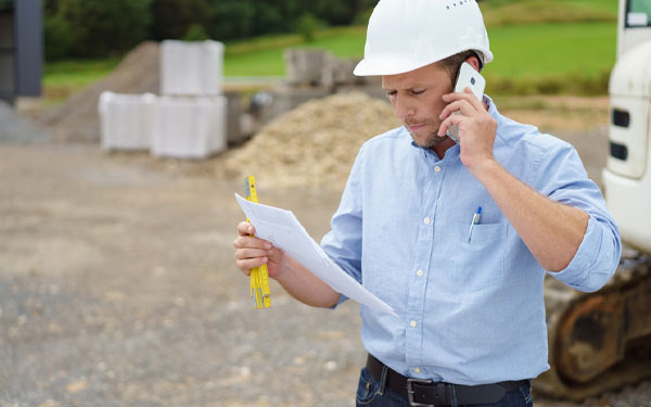 Contractor sitting on jobsite, on a phone call with a lead.