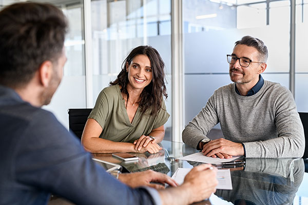 A commercial roofing contractor sits across a table from a smiling woman and man.