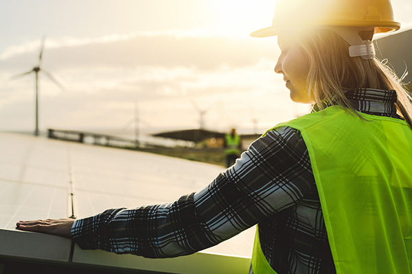 A woman roofer stands in front of solar panels.