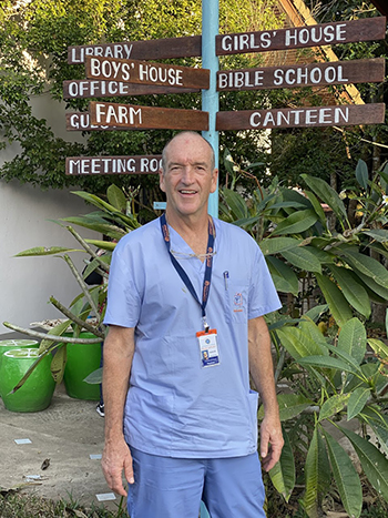 Man in scrubs stands in front of directional sign