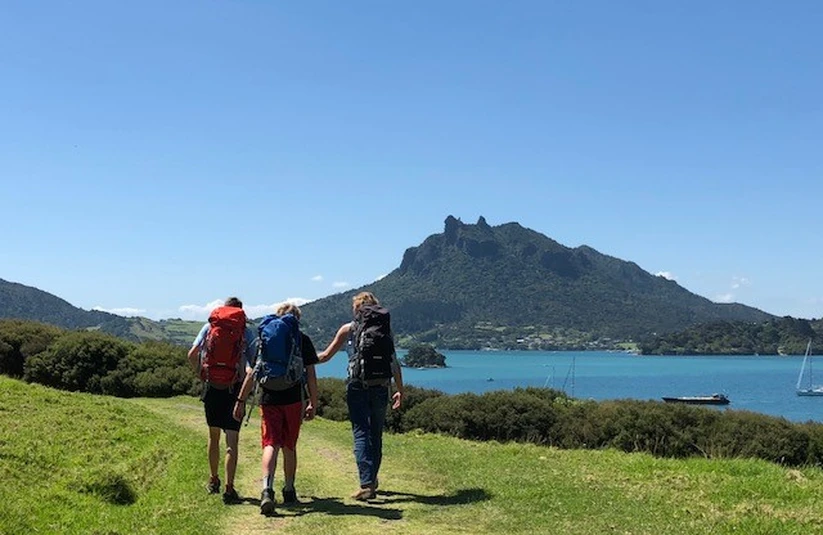 Three people walking toward an ocean bay in New Zealand with a mountain in the background