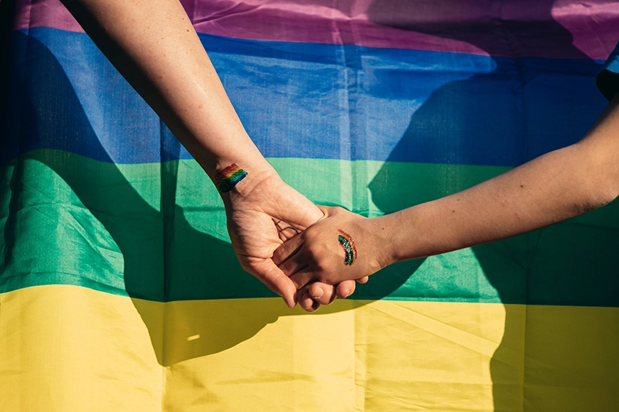 Picture of two people holding hands in front of a Pride flag