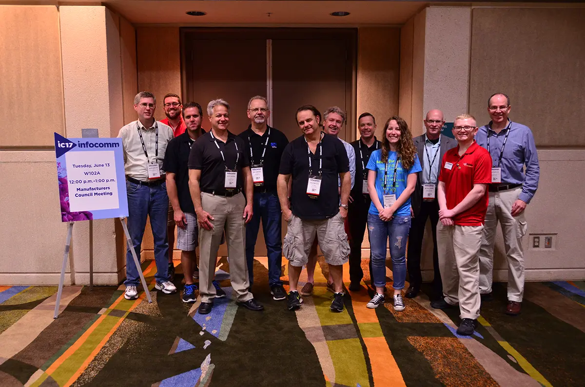 Group of twelve people standing in a conference room with lanyards, posing for a photo next to an InfoComm sign.