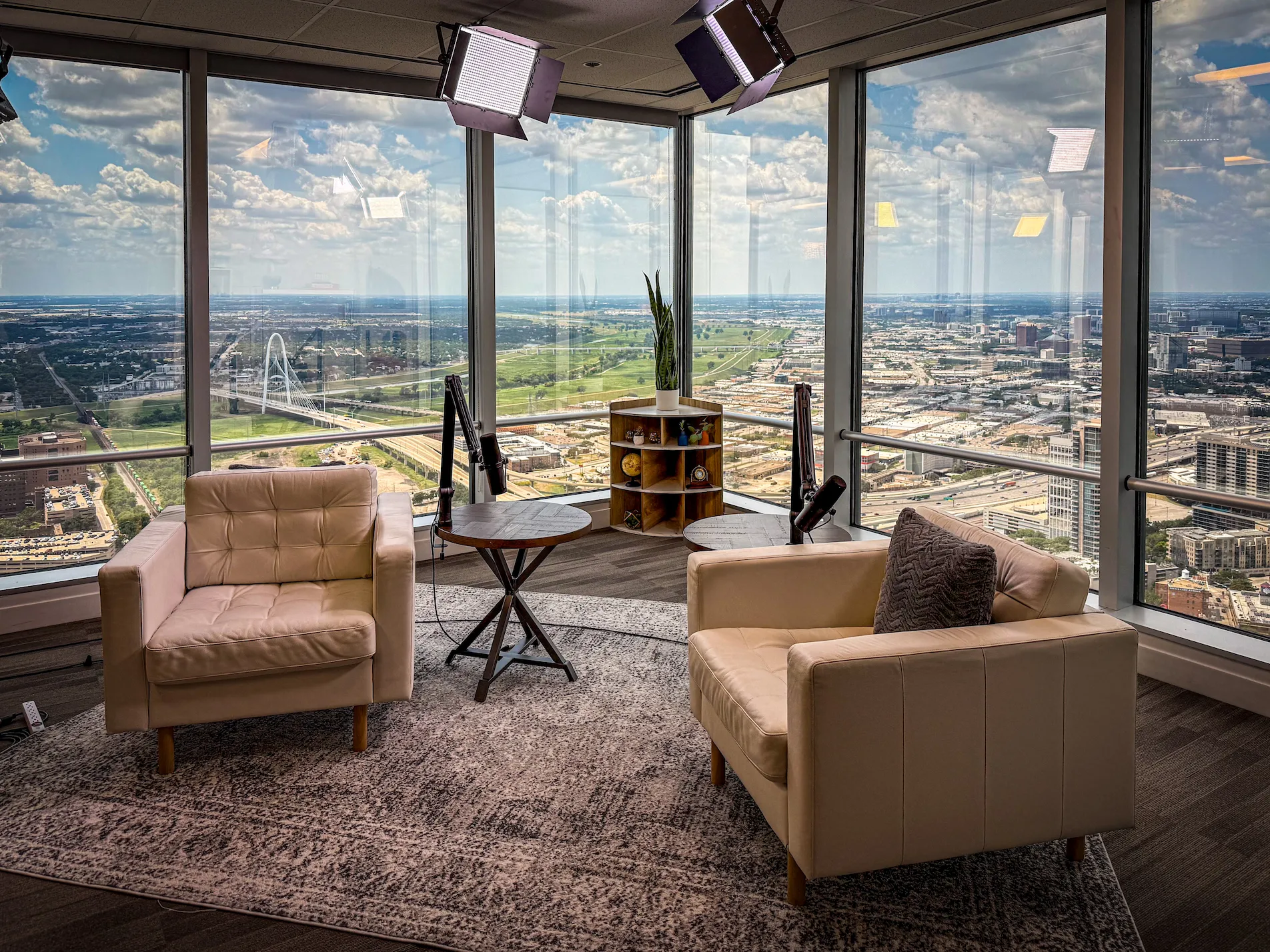 Modern office with two cream chairs, a small table, and large windows offering a panoramic city view under a cloudy sky.