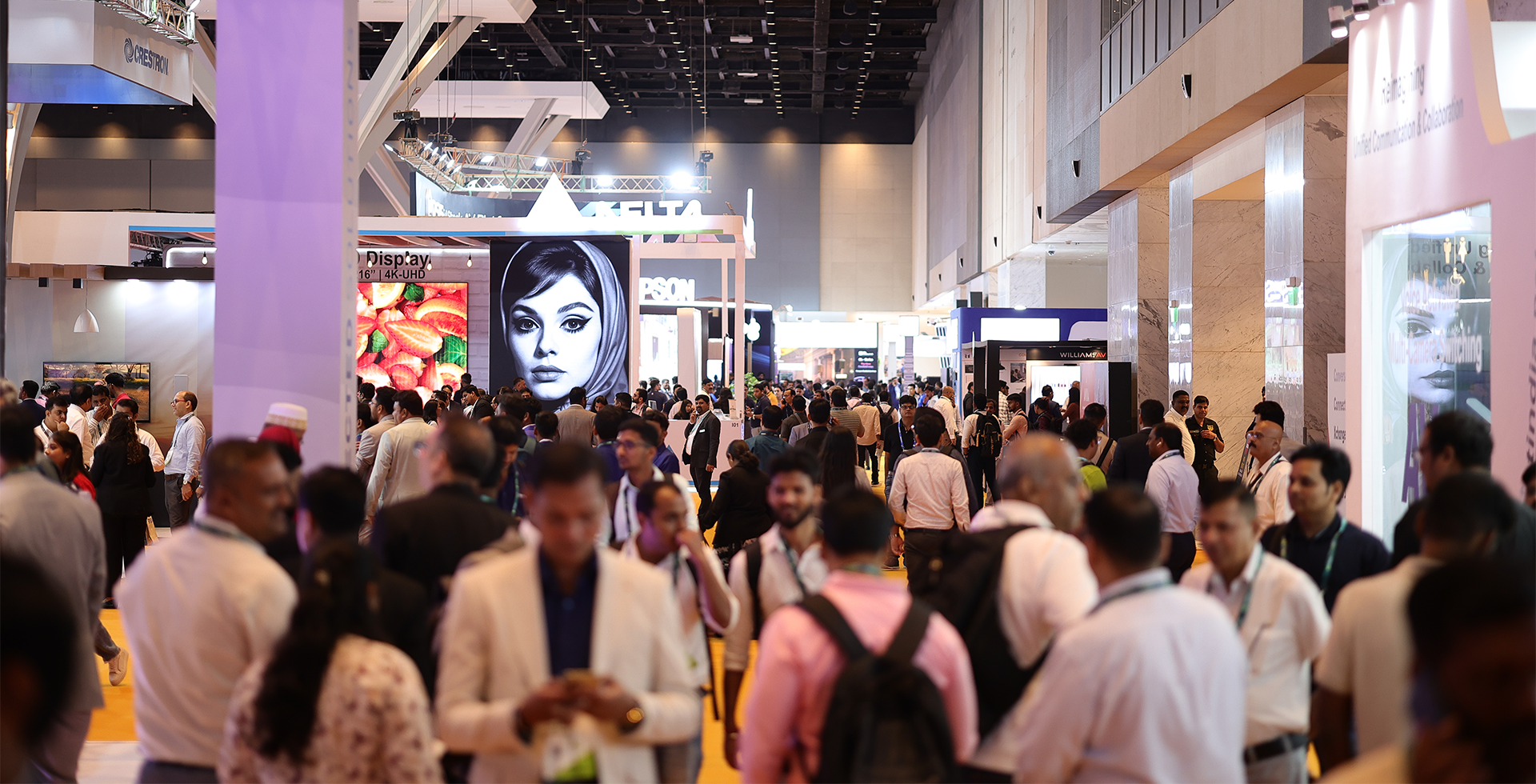 A bustling convention hall filled with people, banners, and digital screens showcasing various technology displays.