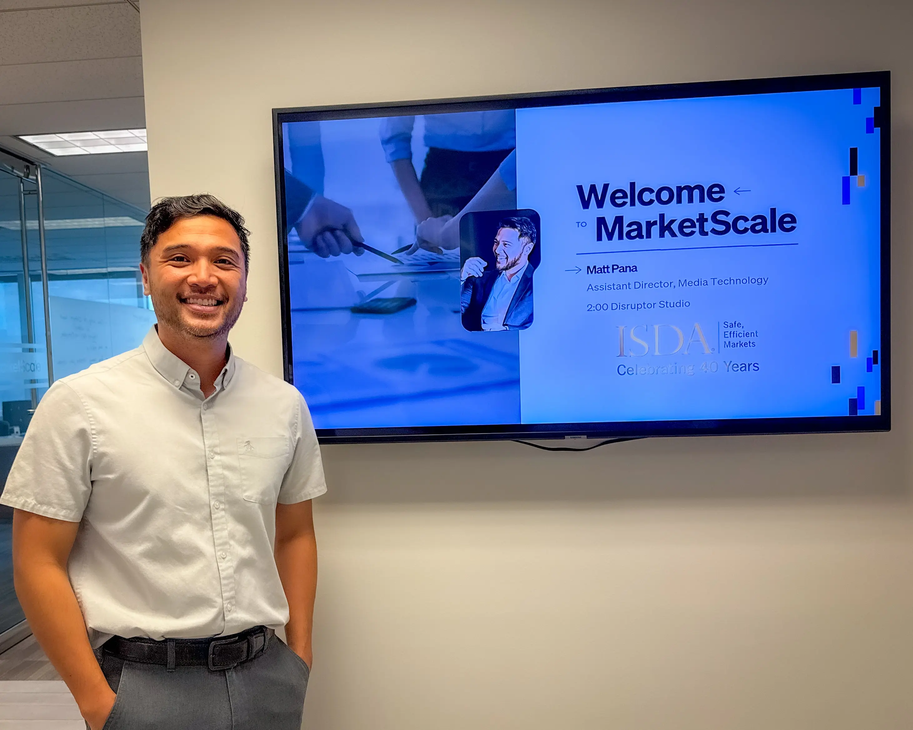 Man smiling next to a monitor displaying a welcome message for MarketScale in an office setting.