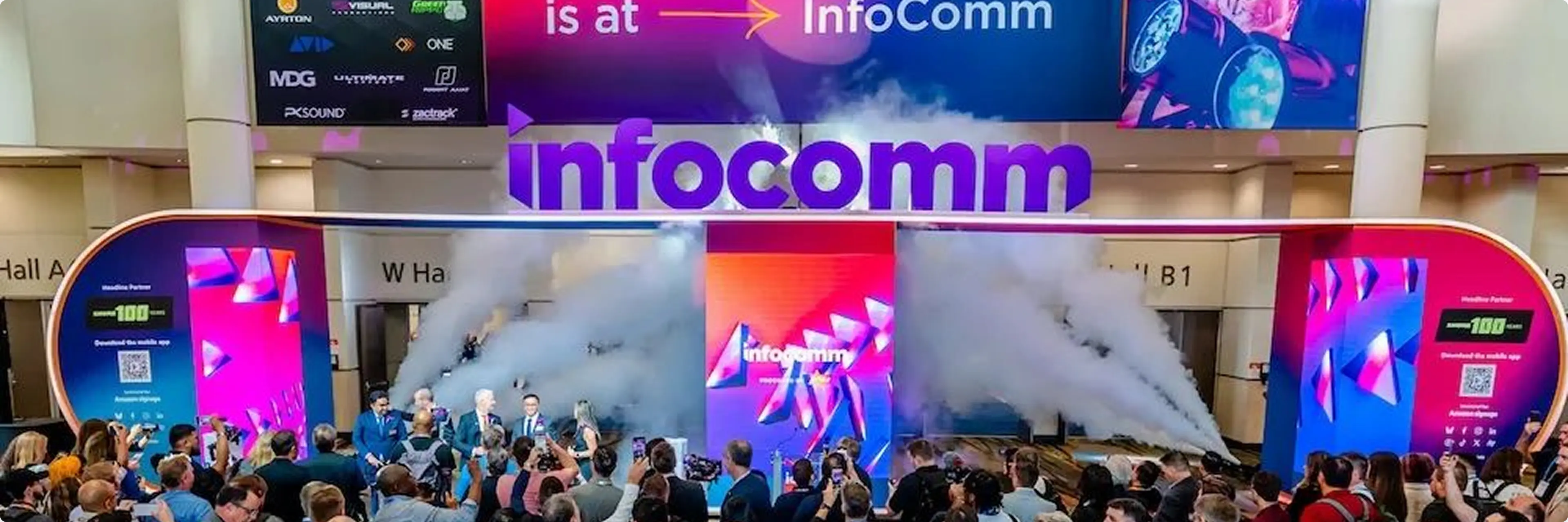 Crowd gathers at the InfoComm entrance, surrounded by colorful screens and smoke effects, for the event's opening.