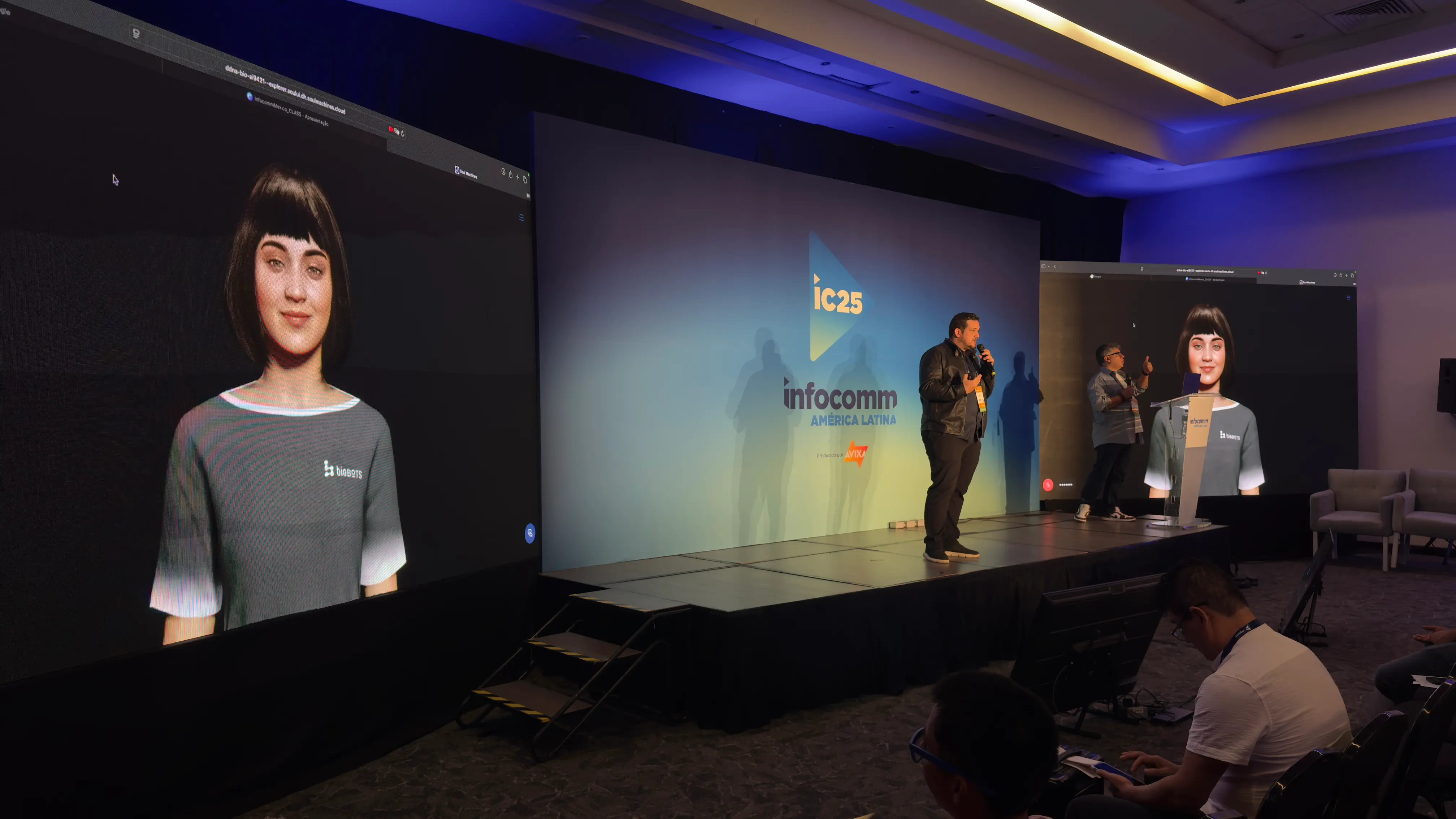 Presenter on stage at InfoComm, with virtual AI assistant displayed on large screens to both sides.