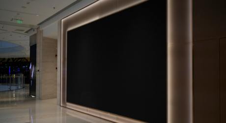 Large black screen on a modern mall wall with surrounding soft lights, reflecting a polished marble floor.