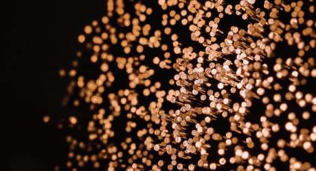 Abstract image of numerous small, glowing orange dots scattered on a dark background, resembling bokeh or fiber optic lights.