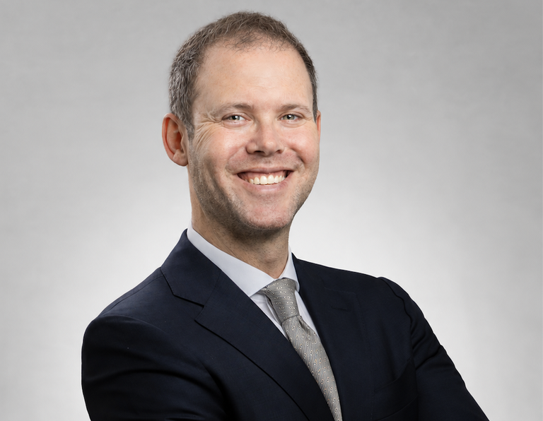 Smiling man in a suit and tie with a light grey background.