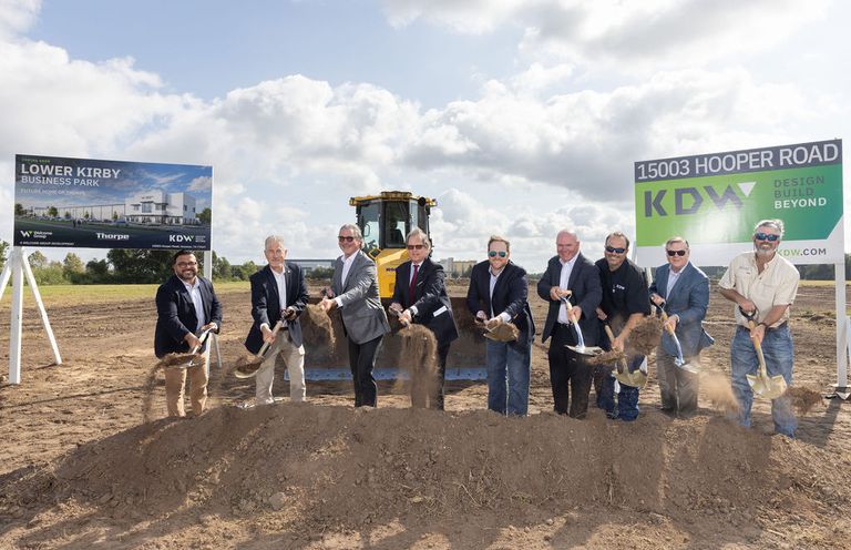 Group of men with shovels breaking ground at the Lower Kirby Business Park site, with construction equipment and signs in the background.