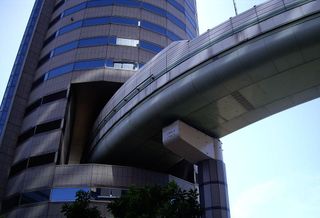 This building is easily recognized by the Hanshin Expressway onramp located within (yes, within) the tower. In the early 1980s, redevelopment of the was approved by the city but building permits stalled because the highway was in planning. Property rights holders negotiated with the Hanshin Expressway for five years before agreeing to jointly develop Gate Tower Building and the highway. 