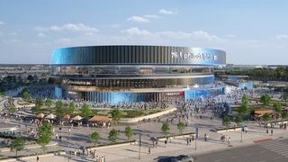 A modern, circular arena with a reflective facade and a bustling plaza, featuring people, cars, and greenery under a clear blue sky.