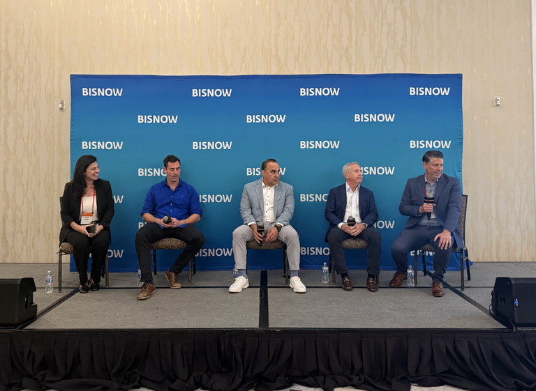 Five people seated on a stage with microphones, in front of a "Bisnow" branded backdrop, participating in a panel discussion.