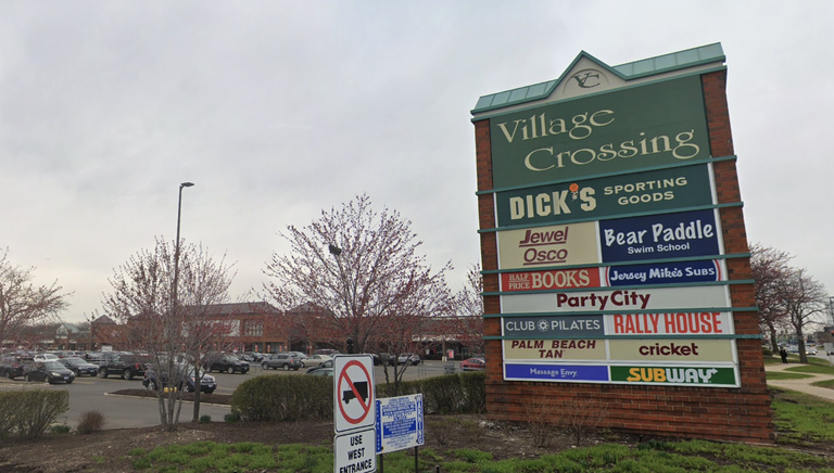 Shopping center sign with various store names, including Dick's Sporting Goods, Party City, and Subway, in a parking lot setting.