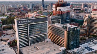 Aerial view of Penn Medicine building in Philadelphia, surrounded by other high-rise structures and ongoing construction, with a cityscape backdrop.