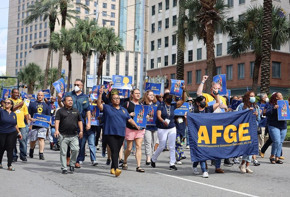 Workers march on a street behind a banner that reads