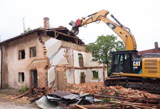 Heavy machinery tears down a house. Demolition is a cheaper way to tear down a building, but it wastes far more carbon than deconstruction.
