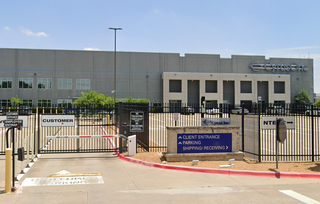Industrial building with "CyrusOne" signage, fenced entrance, labeled for customer and client entry. Signs indicate no tailgating and directions for parking.