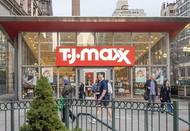 Entrance of a T.J.Maxx store with people walking by on a city street.
