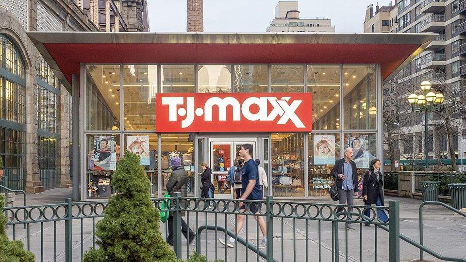 Entrance of a T.J.Maxx store with people walking by on a city street.