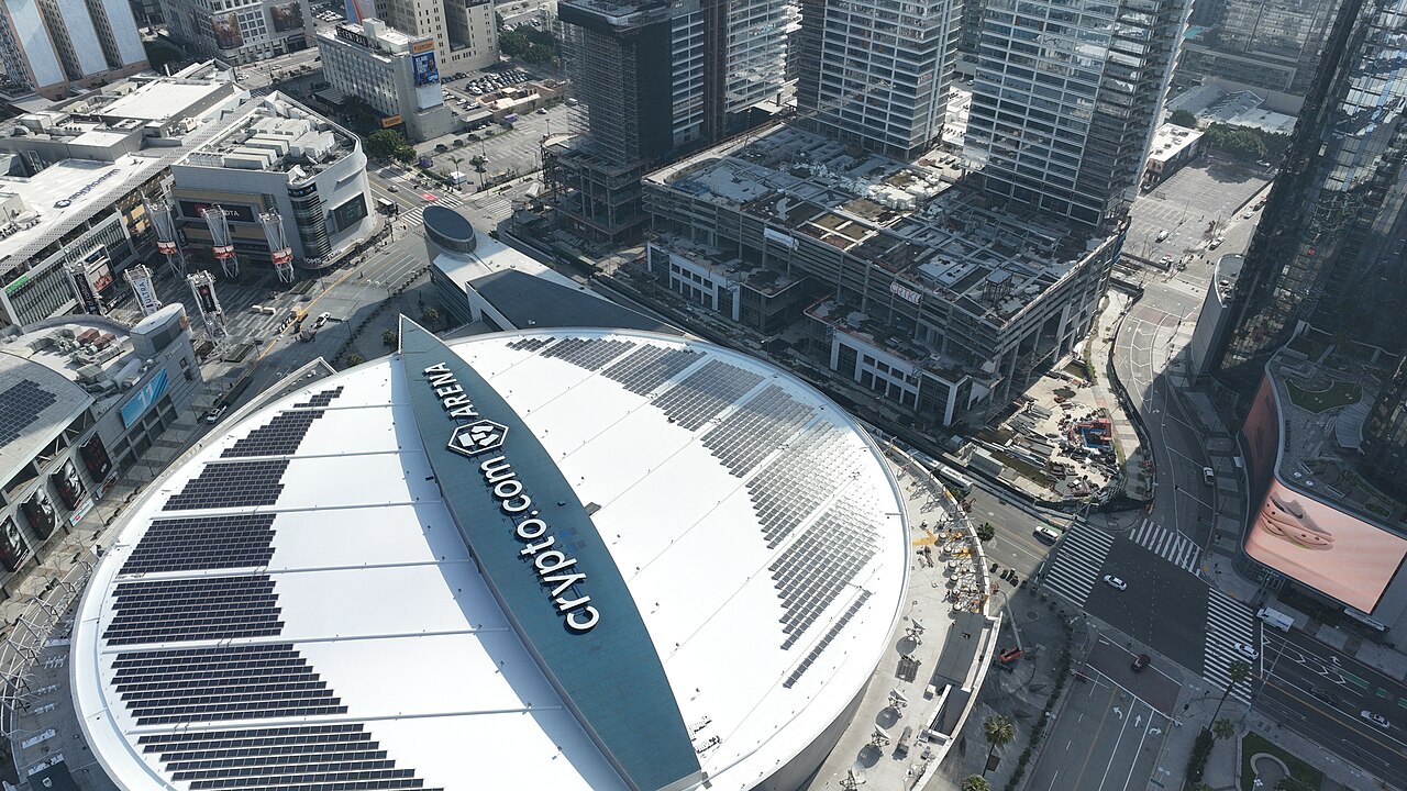 Aerial view of the Crypto.com Arena roof with solar panels, surrounded by urban buildings and roads in Downtown LA.