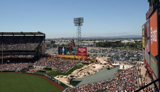 Angels baseball stadium with a packed crowd, large scoreboard, outfield rock feature, and distant view of mountains under a clear blue sky.