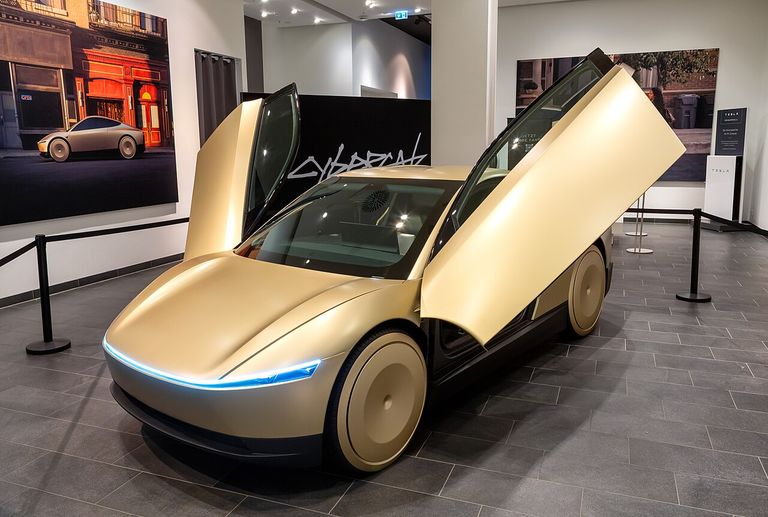 A futuristic gold car with gull-wing doors open on display in a modern showroom, with artwork and branding visible in the background.