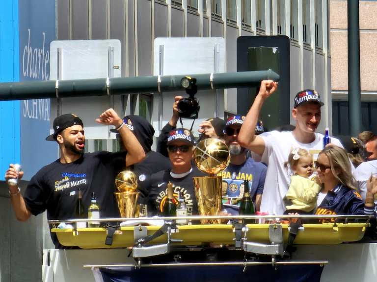 People celebrating on a parade float with golden championship trophies, wearing hats that say "champions".