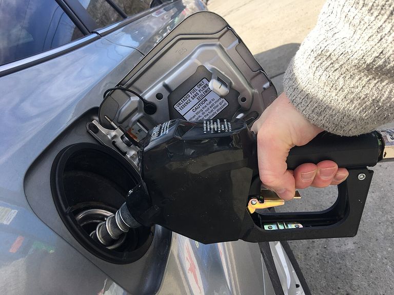Hand refueling a silver car with a black fuel nozzle at a gas station.