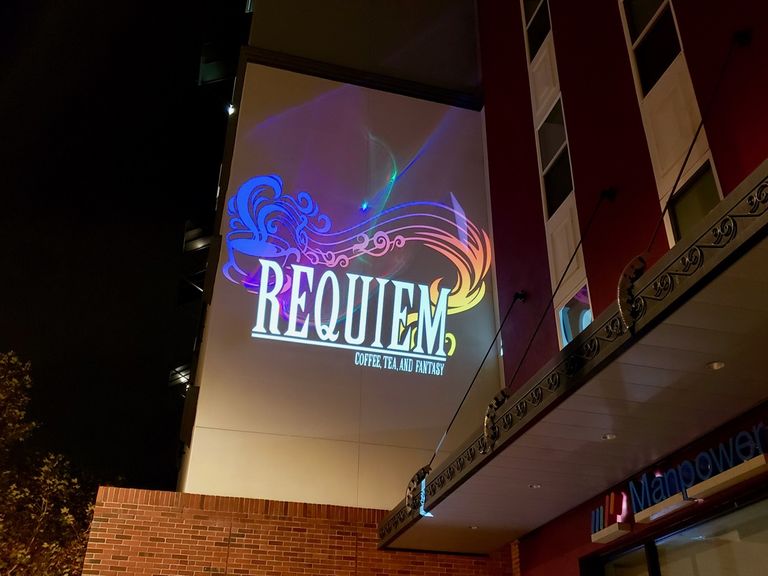 A projector displays a Requiem: Coffee, Tea, and Fantasy against a building wall in Anaheim