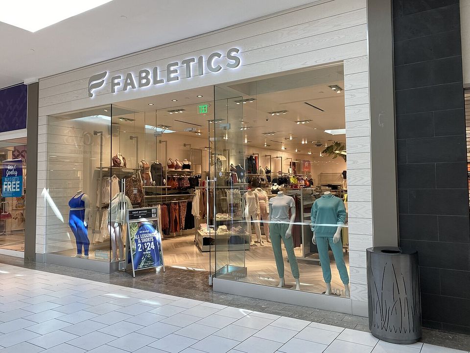 A Fabletics storefront in a mall, featuring mannequins in athleisure and a sign promoting a sale.