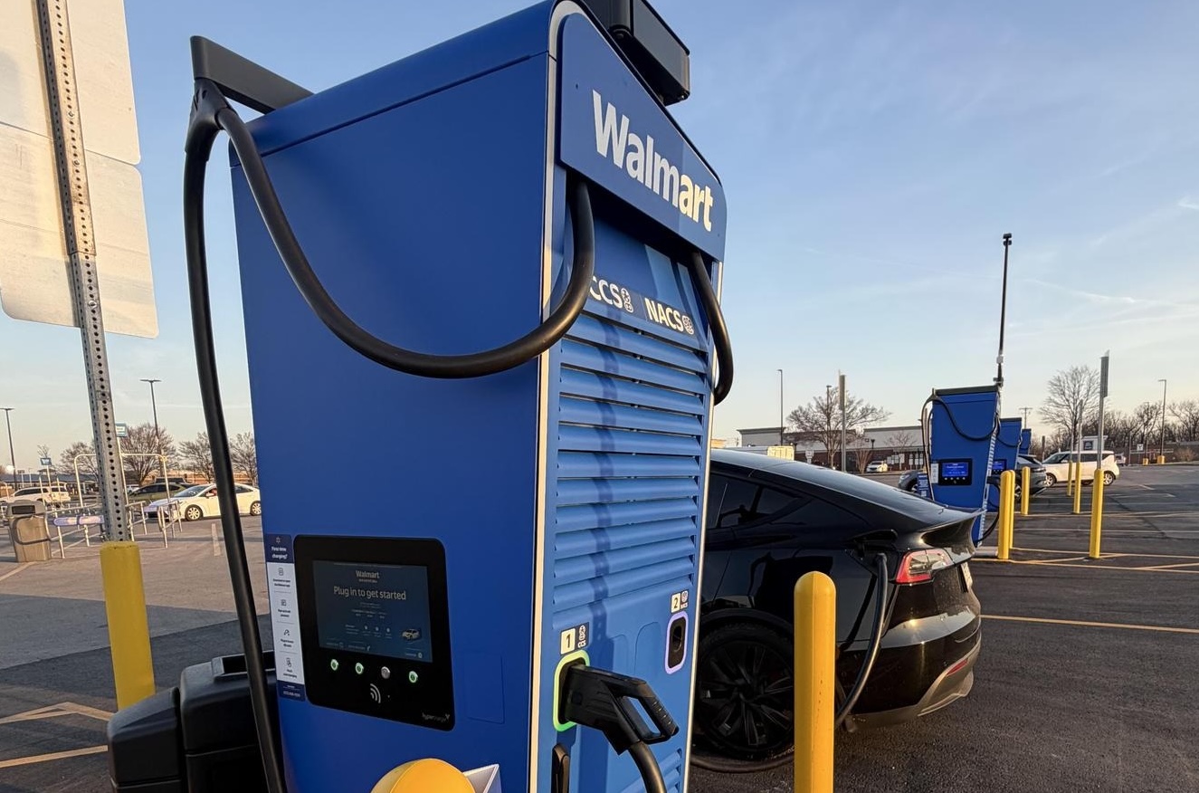 Electric vehicle charging at a Walmart station in a parking lot under a clear sky.