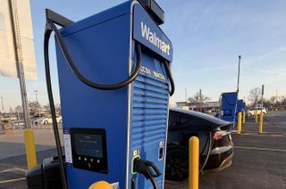 Electric vehicle charging at a Walmart station in a parking lot under a clear sky.