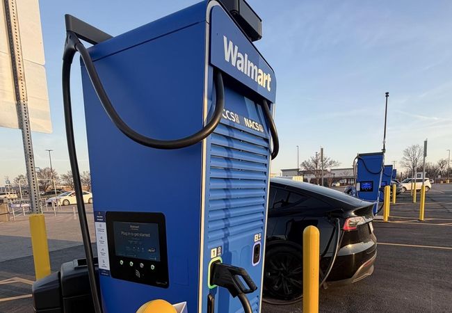 Electric vehicle charging at a Walmart station in a parking lot under a clear sky.