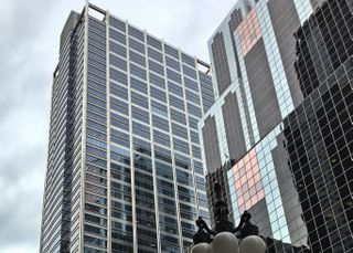 Tall modern skyscrapers with reflective glass facades against a cloudy sky, featuring a street lamp in the foreground.