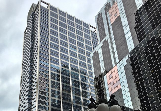Tall modern skyscrapers with reflective glass facades against a cloudy sky, featuring a street lamp in the foreground.